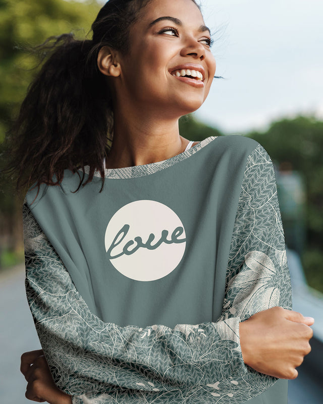 A happy female model is wearing a sweatshirt with the words love over the chest. Her arms are crossed.
